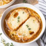 French onion soup topped with cheesy bread in a white bowl.