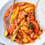 Leczo (Polish stew) in a white bowl with a piece of bread on the side.