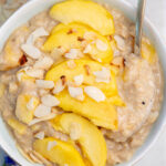 Peach oatmeal in a white bowl topped with peach slices and almond flakes.