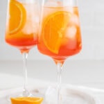 Two glasses with Aperol Spritz cocktail garnished with orange slices.