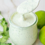 Cilantro lime crema in a jar. Cilantro and limes in the background.