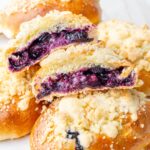 Jagodzianki Polish buns on a white plate. One bun is cut in half showing blueberry filling.