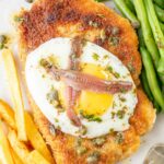 Schnitzel Holstein topped with fried egg, anchovies, and capers on a plate.