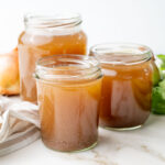 Three jars with beef stock on a marble counter.