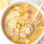 Lemon chicken orzo soup in a beige bowl with two lemon slices on top.